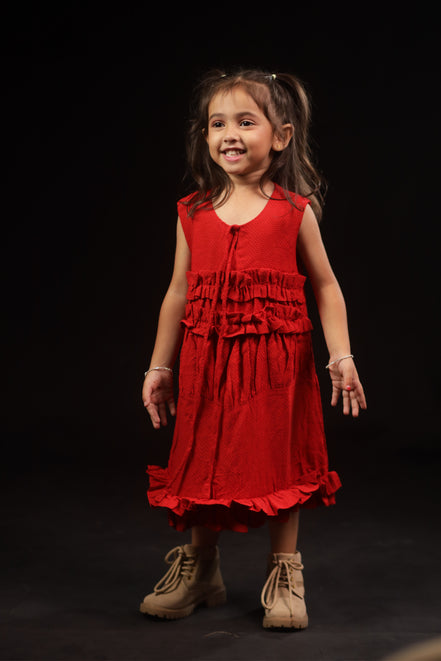 Primrose · Edition Two — girl in a deep scarlet eucalyptus fibre frock holding coloured balls, showing the tiered ruffle bodice