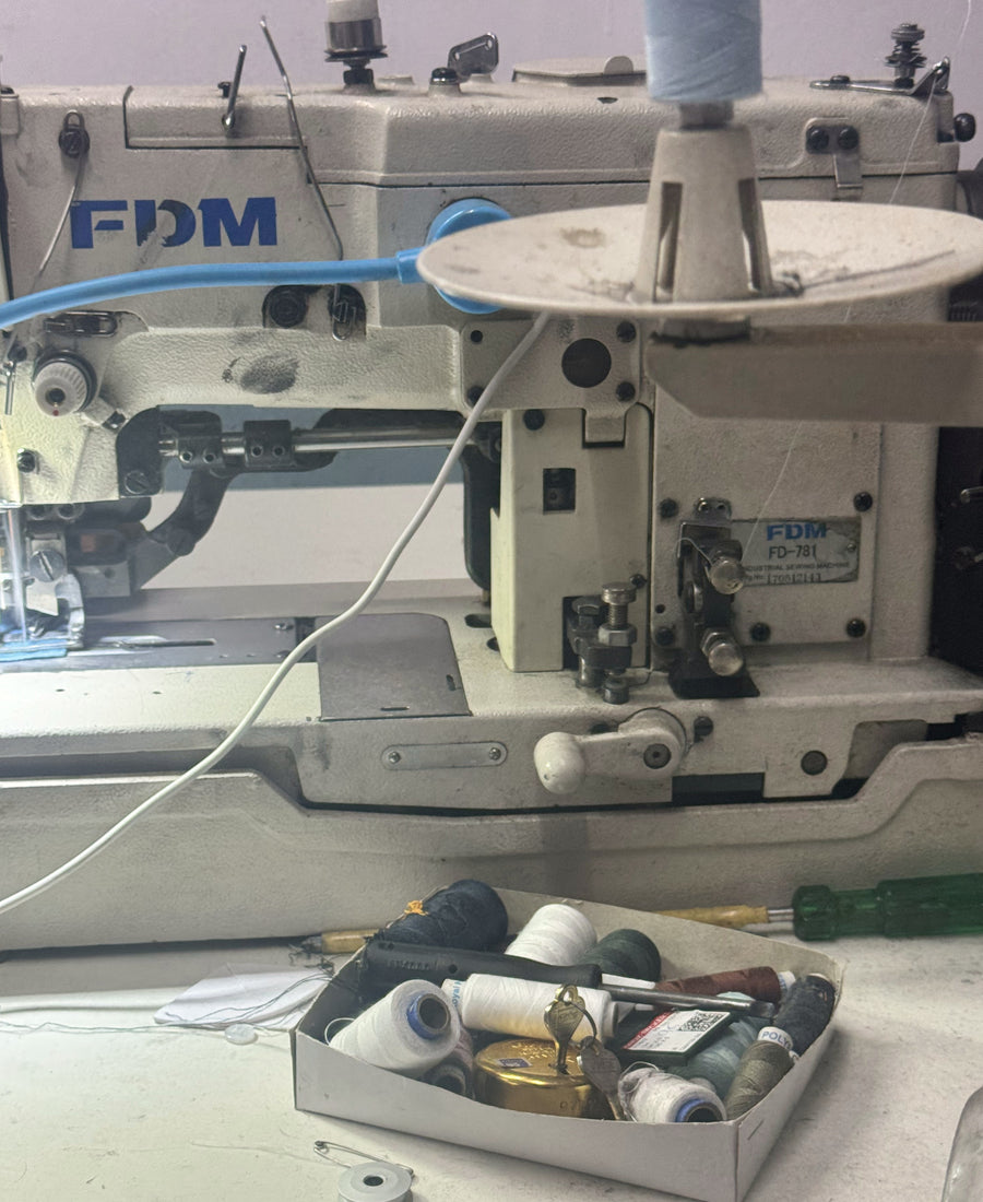 An industrial sewing machine in the Zouhi workshop outside Kochi, with a tray of thread spools and bobbins beside it.